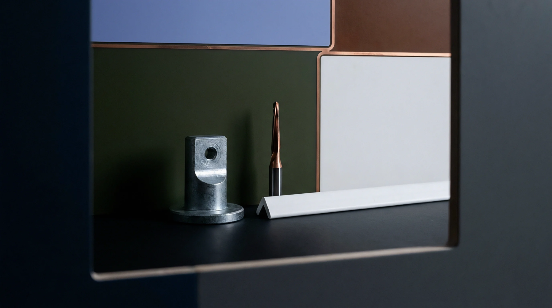 A machined metal connector component, a tapered metal cutting tool, and a white L-profile strip rest on a dark surface against colored panels.