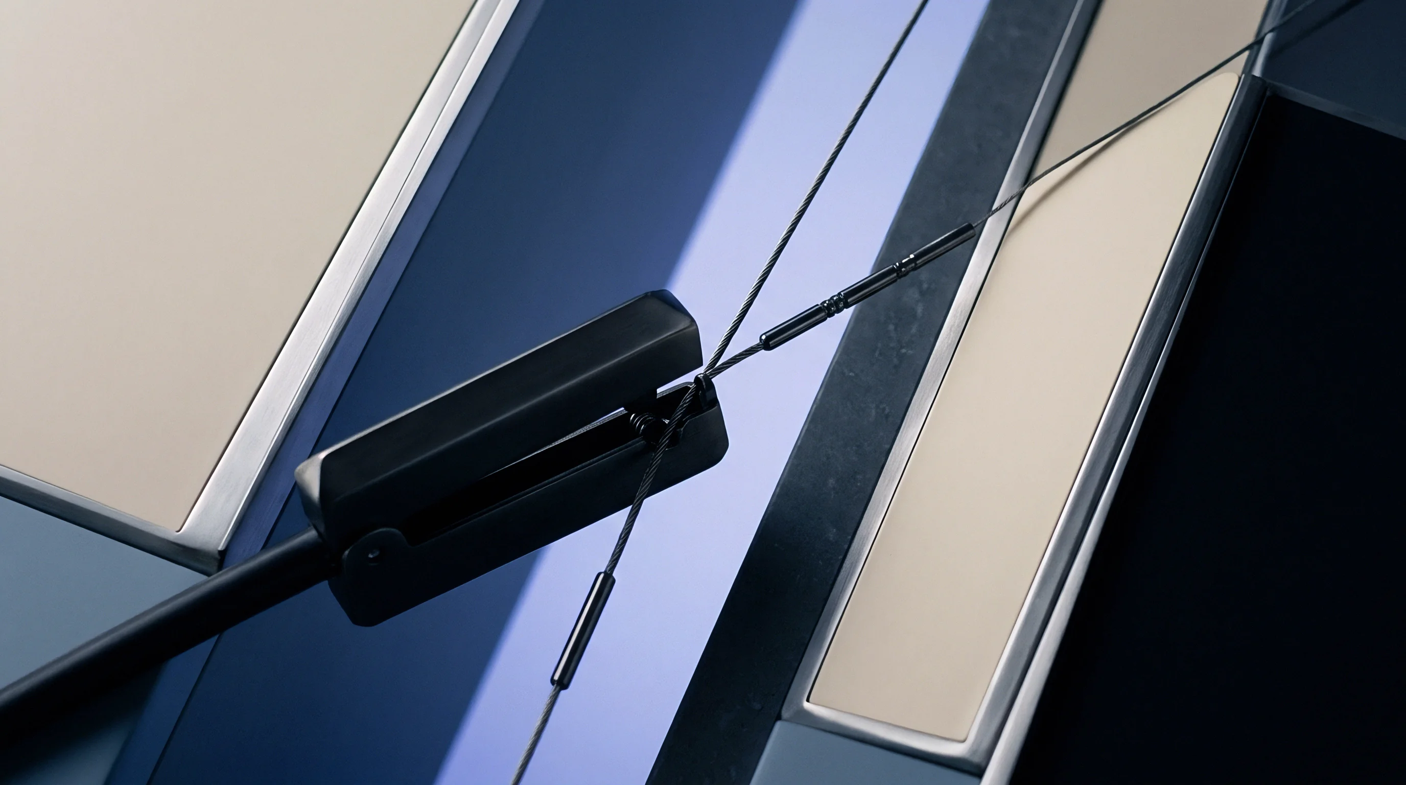 Thin steel wire cables with metal crimp terminals pass through an open black clamp mounted on a geometric background.